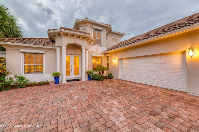 mediterranean / spanish house with an attached garage, decorative driveway, stucco siding, and a tiled roof