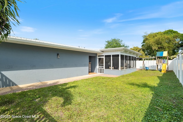back of property featuring a playground, fence, a yard, stucco siding, and a sunroom