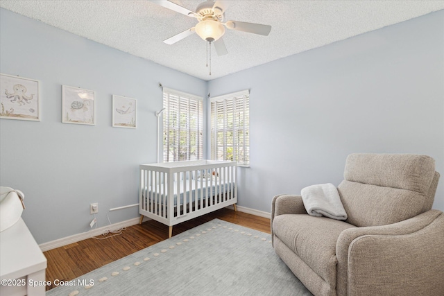 1609 Pga Blvd, Melbourne, FL 32935 - bedroom featuring wood finished floors, a textured ceiling, a crib, ceiling fan, and baseboards