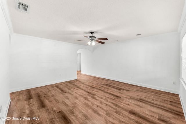 empty room featuring visible vents, arched walkways, ornamental molding, wood finished floors, and a ceiling fan