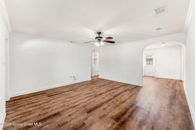 spare room featuring arched walkways, wood finished floors, ornamental molding, visible vents, and a ceiling fan