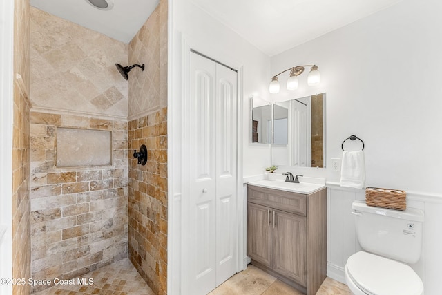 bathroom featuring vanity, a closet, toilet, a tile shower, and wainscoting