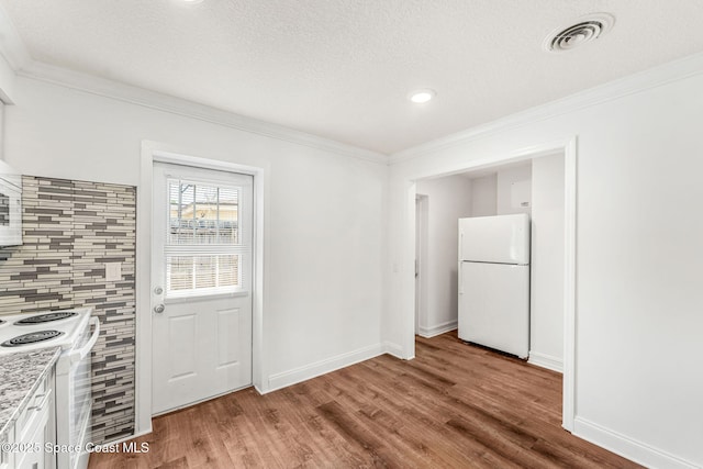 unfurnished dining area featuring crown molding, visible vents, baseboards, a textured ceiling, and wood finished floors
