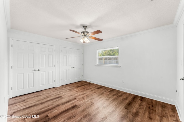 unfurnished bedroom with multiple closets, crown molding, baseboards, a textured ceiling, and wood finished floors