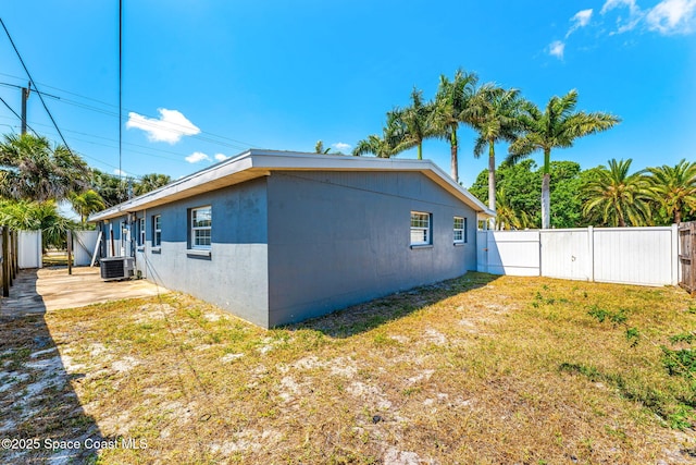 view of side of property with cooling unit, a gate, a lawn, stucco siding, and a fenced backyard