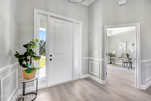 entryway with wood finished floors, a decorative wall, and wainscoting