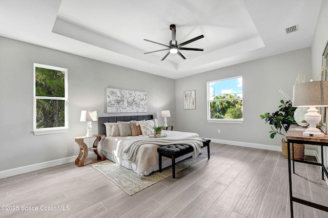 bedroom with light wood finished floors, visible vents, a tray ceiling, and baseboards