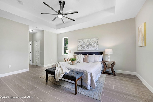bedroom featuring wood finished floors, a ceiling fan, a tray ceiling, and baseboards