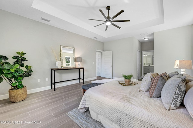 bedroom featuring ensuite bath, baseboards, visible vents, wood tiled floor, and a tray ceiling