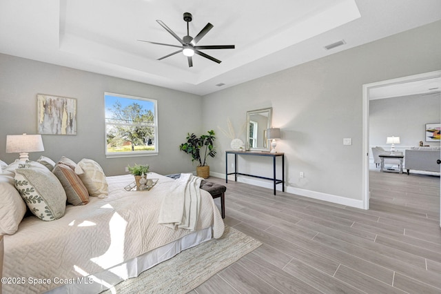 bedroom with wood finished floors, baseboards, visible vents, a ceiling fan, and a tray ceiling