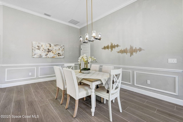 dining room with wood finished floors, an inviting chandelier, crown molding, and a decorative wall