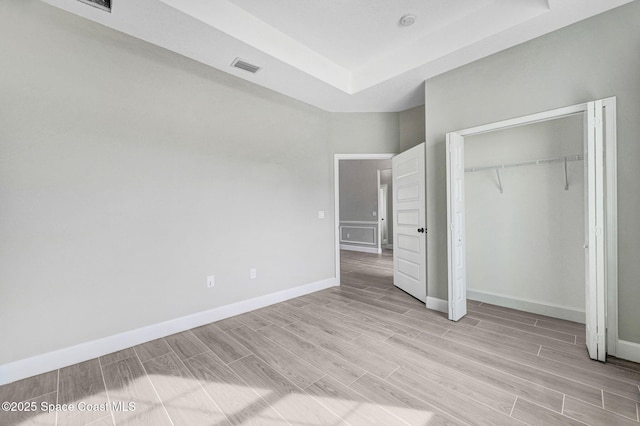 unfurnished bedroom featuring visible vents, a tray ceiling, baseboards, a closet, and wood finish floors
