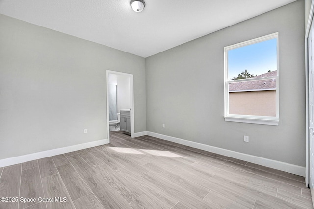 unfurnished bedroom featuring wood finished floors, ensuite bath, and baseboards