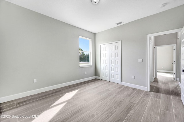 unfurnished bedroom featuring wood finished floors, visible vents, a closet, and baseboards