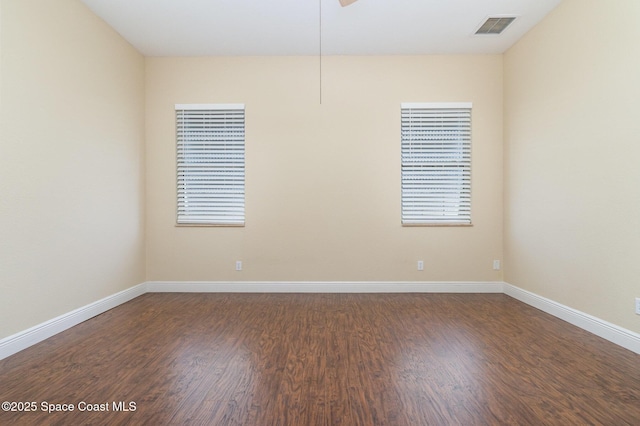 empty room with baseboards, visible vents, and dark wood finished floors