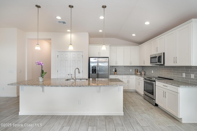 kitchen featuring appliances with stainless steel finishes, a sink, vaulted ceiling, tasteful backsplash, and light wood-type flooring