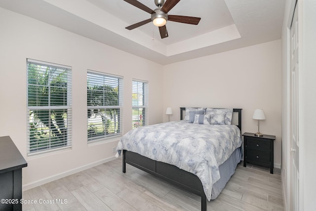 bedroom with a tray ceiling, a ceiling fan, baseboards, and light wood-style flooring
