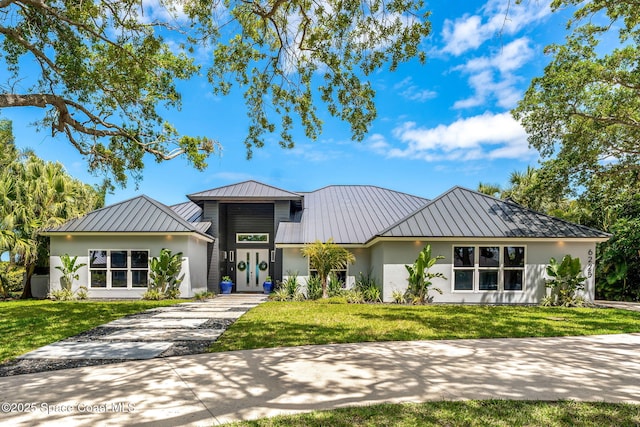 view of front of property with a standing seam roof, stucco siding, metal roof, a front lawn, and driveway
