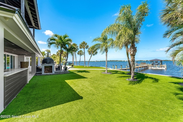 view of green lawn featuring exterior fireplace, a water view, and a patio