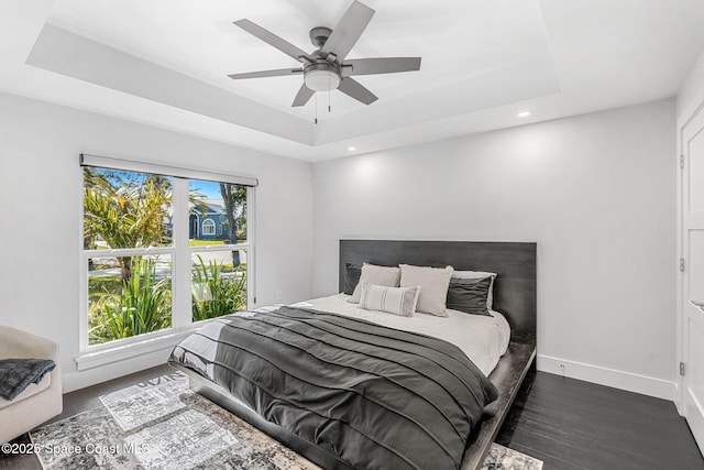 bedroom with a tray ceiling, wood finished floors, baseboards, recessed lighting, and a ceiling fan