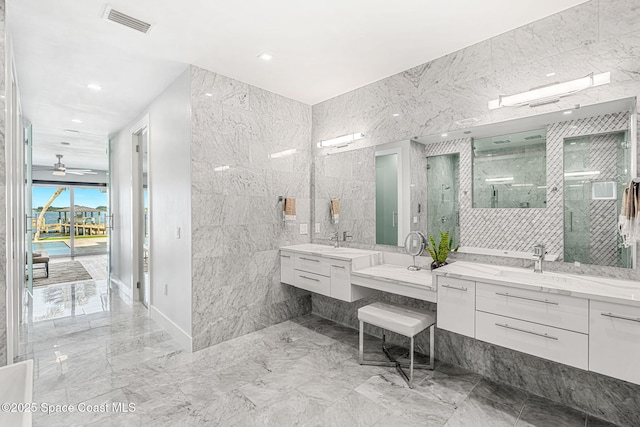 bathroom with marble tiled floors, two vanities, tile walls, a shower stall, and recessed lighting