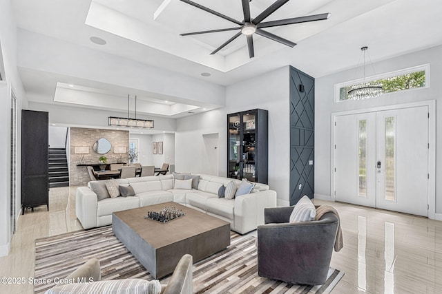 living area featuring a raised ceiling, a chandelier, a ceiling fan, baseboards, and light tile patterned floors