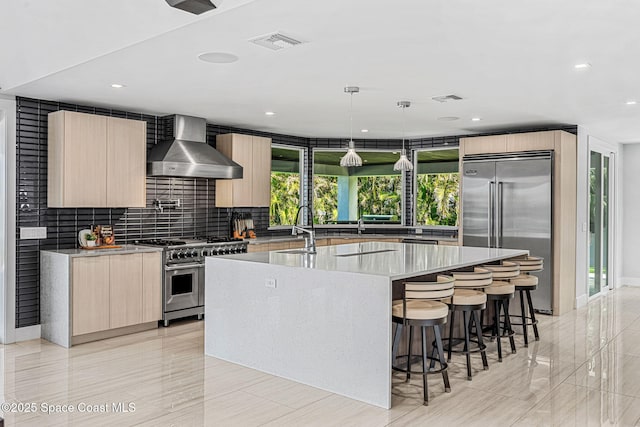 kitchen with high quality appliances, modern cabinets, wall chimney exhaust hood, a sink, and a spacious island