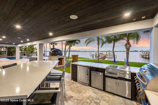 view of patio / terrace featuring exterior kitchen, a grill, a water view, and a bar