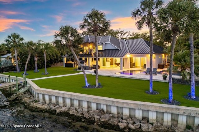 rear view of house with a balcony, a patio, a standing seam roof, an outdoor pool, and a water view