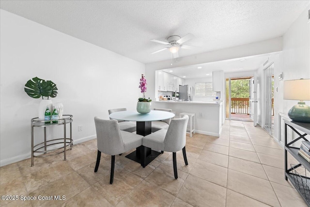 dining space with light tile patterned floors, baseboards, ceiling fan, and a textured ceiling