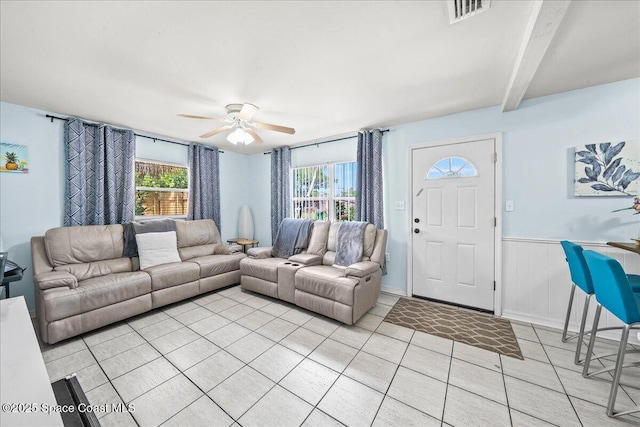 living room featuring a wainscoted wall, visible vents, light tile patterned floors, beam ceiling, and ceiling fan