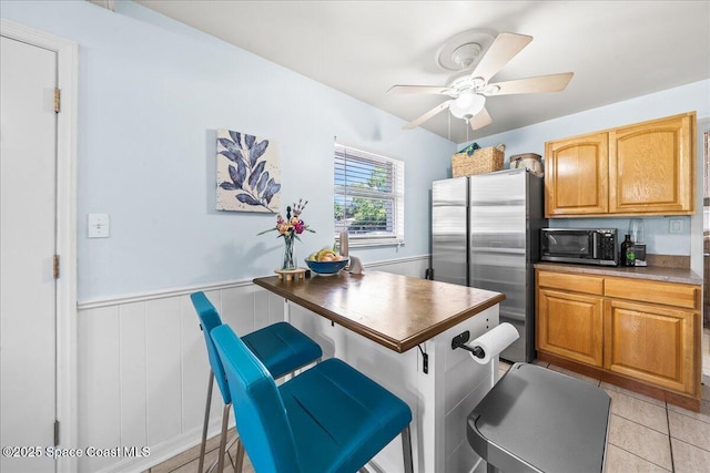 kitchen featuring wainscoting, ceiling fan, appliances with stainless steel finishes, and dark countertops