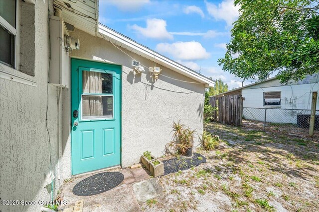 view of exterior entry with stucco siding and fence