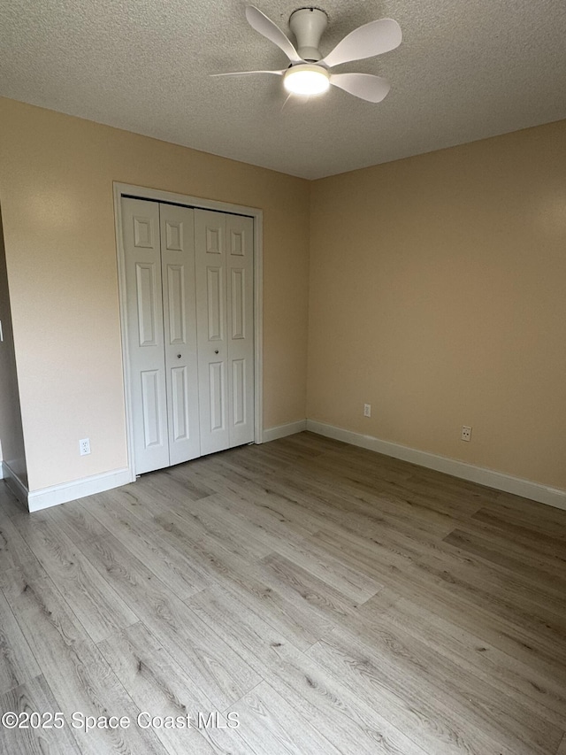 unfurnished bedroom featuring light wood finished floors, a textured ceiling, a closet, baseboards, and ceiling fan