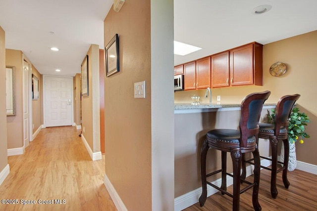 kitchen featuring baseboards, a kitchen bar, light wood-type flooring, recessed lighting, and stainless steel microwave