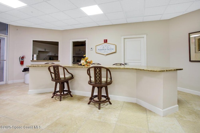 kitchen with a breakfast bar area, light tile patterned flooring, and light stone countertops