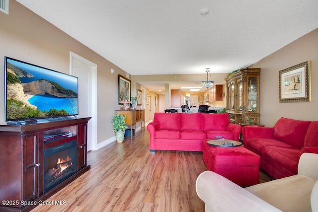 living room featuring visible vents, light wood finished floors, a glass covered fireplace, and baseboards