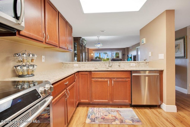 kitchen with a sink, light stone counters, stainless steel appliances, and light wood finished floors