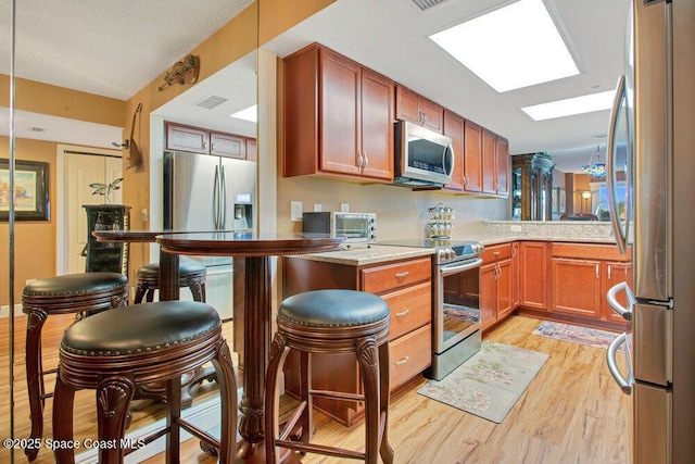 kitchen with appliances with stainless steel finishes, a peninsula, light wood-type flooring, a toaster, and visible vents