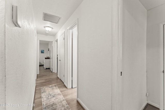 corridor with attic access, light wood-style flooring, visible vents, and baseboards