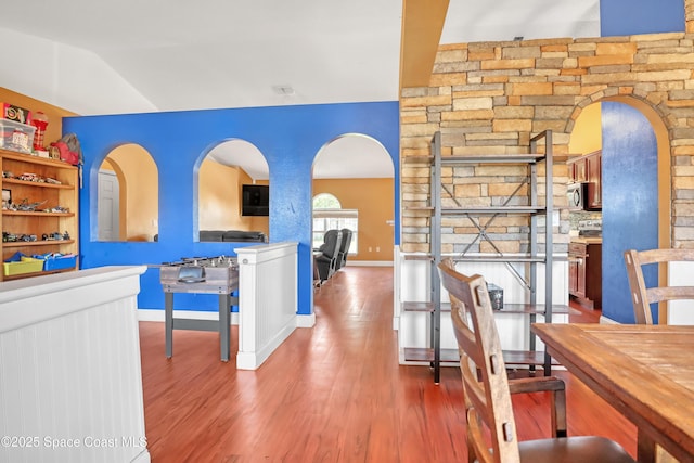 corridor with vaulted ceiling, arched walkways, wood finished floors, and baseboards