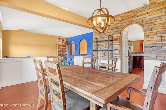 dining room with arched walkways, an inviting chandelier, wood finished floors, and wainscoting