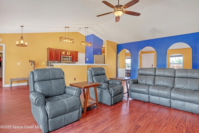 living area with lofted ceiling, wood finished floors, arched walkways, and ceiling fan with notable chandelier