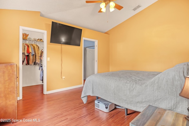 bedroom with wood finished floors, a closet, a walk in closet, lofted ceiling, and visible vents