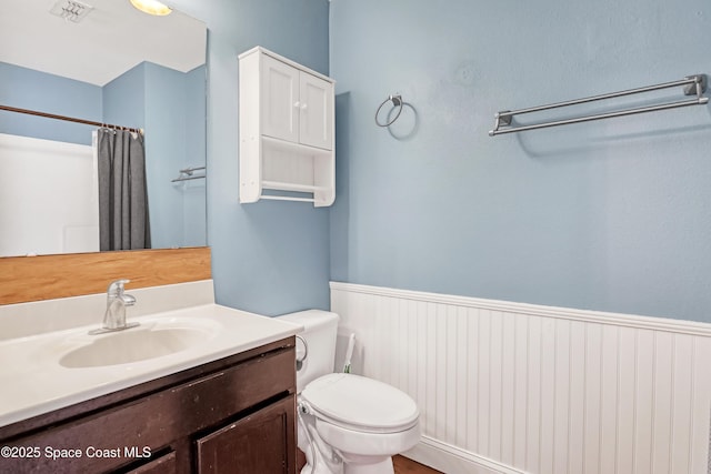 bathroom with vanity, a shower with curtain, a wainscoted wall, toilet, and visible vents