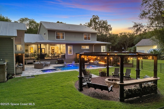 3592 S Park Ave, Titusville, FL 32780 - back of property at dusk with a jacuzzi, an outdoor pool, an outdoor living space with a fire pit, metal roof, and a patio area