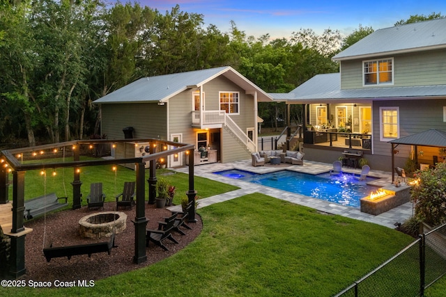 3592 S Park Ave, Titusville, FL 32780 - back of property at dusk featuring an outdoor living space with a fire pit, stairs, an in-ground hot tub, metal roof, and a patio area