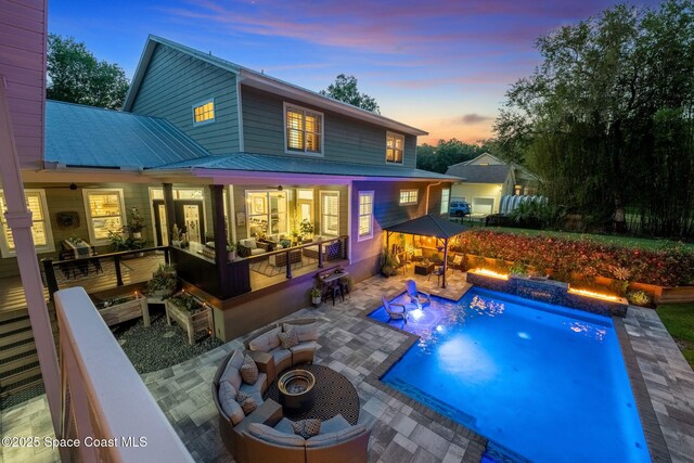 3592 S Park Ave, Titusville, FL 32780 - back of property at dusk with a patio area, an outdoor pool, an outdoor living space with a fire pit, and metal roof
