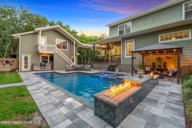 3592 S Park Ave, Titusville, FL 32780 - back of property at dusk featuring an outdoor living space with a fire pit, stairs, a gazebo, a ceiling fan, and an outdoor pool