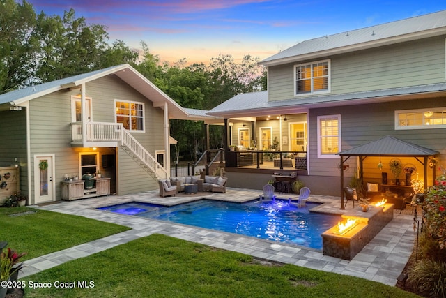 3592 S Park Ave, Titusville, FL 32780 - back of house at dusk featuring stairway, a yard, an outdoor living space with a fire pit, an outdoor pool, and a patio